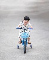 menina asiática sorrindo feliz em andar de bicicleta na estrada, criança andando de bicicleta na estrada, conceito de atividade esportiva de bebê foto