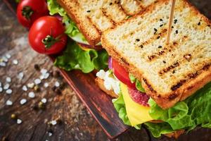 sanduíche caseiro com presunto, alface, queijo e tomate em um fundo de madeira