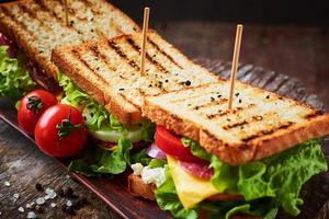 sanduíche caseiro com presunto, alface, queijo e tomate em um fundo de madeira