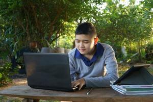 menino está estudando on-line em uma mesa de madeira com um laptop e tablet durante as horas da manhã em uma casa rural. conceito área rural de educação on-line e trabalho em casa foto