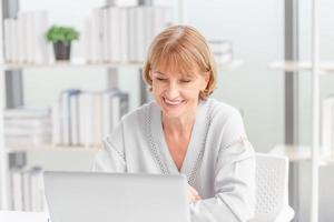 retrato de mulher alegre usando laptop e smartphone em casa, mulher madura na sala de estar com laptop falando videochamada no gadget de computador moderno foto