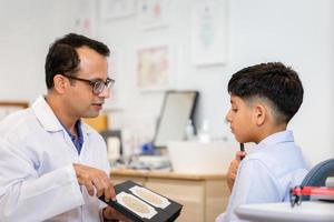 menino fazendo exame de verificação de olho com optometrista na loja de óptica, menino indiano-tailandês na loja de óptica foto