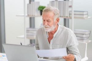 homem sênior preocupado verificando suas contas, família idosa aposentada lendo documentos, homem maduro na sala de estar com laptop foto