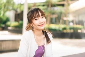 mulher asiática adulta jovem feliz ouvindo streaming de música ao ar livre no dia.