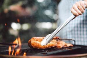 mão de homem grelhando churrasco em chamas no quintal no dia foto