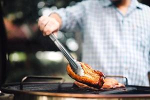 mão de homem grelhando churrasco em chamas no quintal no dia foto