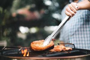 mão de homem grelhando churrasco em chamas no quintal no dia foto