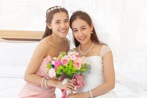 noivas asiáticas em um vestido de noiva branco e damas de honra em um vestido rosa segurando um buquê de rosas juntos e sorrindo brilhantemente. foto