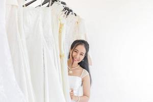 uma noiva asiática está escolhendo um vestido para seu casamento, em pé enviando um sorriso bonito e brilhante. foto