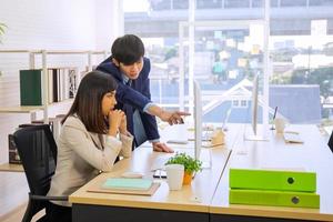 dois funcionários asiáticos masculinos e femininos ajudaram a planejar uma mesa cheia de documentos e tablets, notebooks. foto