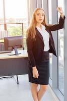 uma bela jovem empresária ao lado de uma parede de vidro em um escritório foto