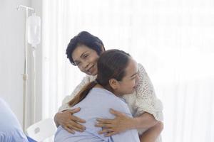 uma jovem asiática que está doente em um hospital abraça sua mãe que cuida dela. foto