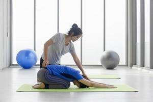 uma treinadora está ensinando uma cliente asiática de meia-idade a fazer ioga em um tapete de borracha em um ginásio. foto