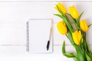 lindas tulipas amarelas, caderno de papel vazio em fundo branco de madeira. foto