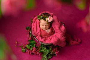 Retrato aproximado de uma linda garota recém-nascida dormindo embrulhada em um cobertor macio roxo, vestindo flor de cabeça estilosa, conceito de moda bebê foto