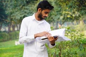 menino indiano com caneta de livros e de pé perto do campus universitário foto