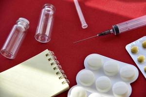 comprimidos de seringa médica e bolhas de vidro em um fundo vermelho