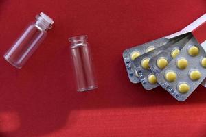 comprimidos de seringa médica e bolhas de vidro em um fundo vermelho
