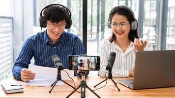podcasters asiáticos de homem e mulher em fones de ouvido gravando conteúdo com colega falando com microfone e câmera no estúdio de transmissão juntos, tecnologia de comunicação e conceito de entretenimento. foto