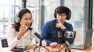 podcasters asiáticos de homem e mulher em fones de ouvido gravando conteúdo com colega falando com microfone e câmera no estúdio de transmissão juntos, tecnologia de comunicação e conceito de entretenimento