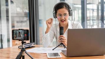 podcaster de mulheres asiáticas podcasting e gravação de talk show on-line no estúdio usando fones de ouvido, microfone profissional e laptop de computador na mesa olhando para a câmera para podcast de rádio