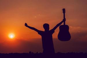 a silhueta de um guitarrista que segura uma guitarra e tem um pôr do sol, conceito de silhueta. foto