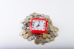 dinheiro, moedas de baht em um fundo branco e um relógio vermelho foto