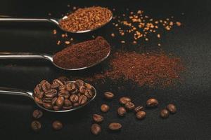 três colheres de café com café solúvel, grãos de café e café moído em fundo escuro foto