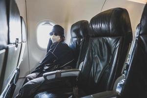 viajante de mulher com máscara médica e óculos de sol sentado no assento do avião foto