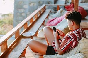 jovem relaxando no saco de feijão na varanda e jogando smartphone foto