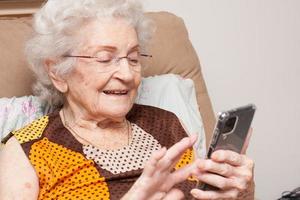 senhora idosa em casa sentada em uma cadeira olhando para seu smartphone foto
