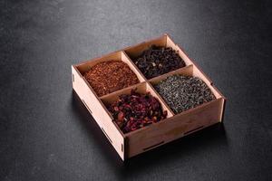 vários tipos de chá preto seco com bergamota, rooibos, verde e moldura em uma caixa de madeira em um fundo preto de concreto foto