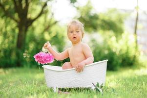 menina criança feliz toma um banho de leite com pétalas. menina em um banho de leite sobre um fundo verde. buquês de peônias rosa. banho do bebê. higiene e cuidados com as crianças. foto