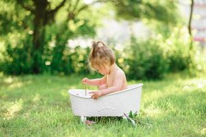menina criança feliz toma um banho de leite com pétalas. menina em um banho de leite sobre um fundo verde. buquês de peônias rosa. banho do bebê. higiene e cuidados com as crianças. foto