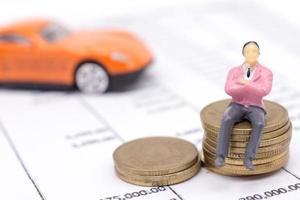 empresário em miniatura e empilhar moedas na declaração e o carro atrás. conceito de poupança e empréstimo. foto
