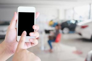 mãos segurando o celular com carros novos no showroom foto