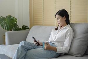 jovem mulher feliz relaxando e usando telefone inteligente em casa, mídia social e conceito de tecnologia. foto