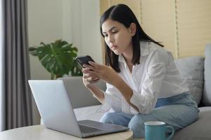 jovem mulher feliz relaxando e usando telefone inteligente em casa, mídia social e conceito de tecnologia. foto