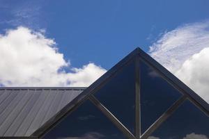 parte do telhado triangular de uma casa de madeira moderna contra o céu brilhante ao fundo.