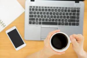 laptop e mão segurando a xícara de café
