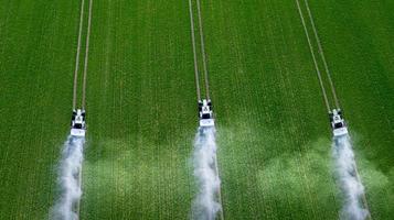 três tratores pulverizam pesticidas em uma vista superior de campo verde foto