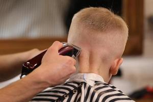 penteado masculino, corte de cabelo, em uma barbearia ou salão de cabeleireiro. close-up de mãos de homem aliciamento de cabelo de menino garoto na barbearia. menino cortado com máquina de cabeleireiro. foto