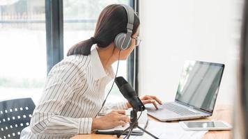 podcaster de mulheres asiáticas podcasting e gravação de talk show on-line no estúdio usando fones de ouvido, microfone profissional e laptop de computador na mesa olhando para a câmera para podcast de rádio.