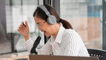 podcaster de mulheres asiáticas podcasting e gravação de talk show on-line no estúdio usando fones de ouvido, microfone profissional e laptop de computador na mesa olhando para a câmera para podcast de rádio