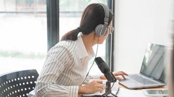 podcaster de mulheres asiáticas podcasting e gravação de talk show on-line no estúdio usando fones de ouvido, microfone profissional e laptop de computador na mesa olhando para a câmera para podcast de rádio.