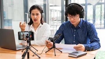 podcasters asiáticos de homem e mulher em fones de ouvido gravando conteúdo com colega falando com microfone e câmera no estúdio de transmissão juntos, tecnologia de comunicação e conceito de entretenimento. foto