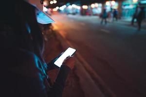 ela usa smartphone para transporte de táxi na rua comercial à noite. foto