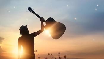 músico segurando a guitarra na mão da silhueta no fundo da natureza por do sol foto
