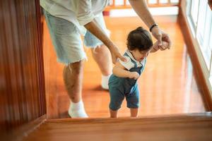 criança bonitinha conceito de família criança, bebê aprendendo a andar com pai e mãe para ajudar a cuidar e segurar a mão, primeiro passo com apoio dos pais na infância, pequeno retrato de amor menino em casa foto