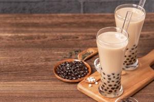 bebida popular de taiwan - chá de leite bolha com bola de pérola de tapioca em copo e palha, mesa de madeira fundo de tijolo cinza, close-up, copie o espaço foto